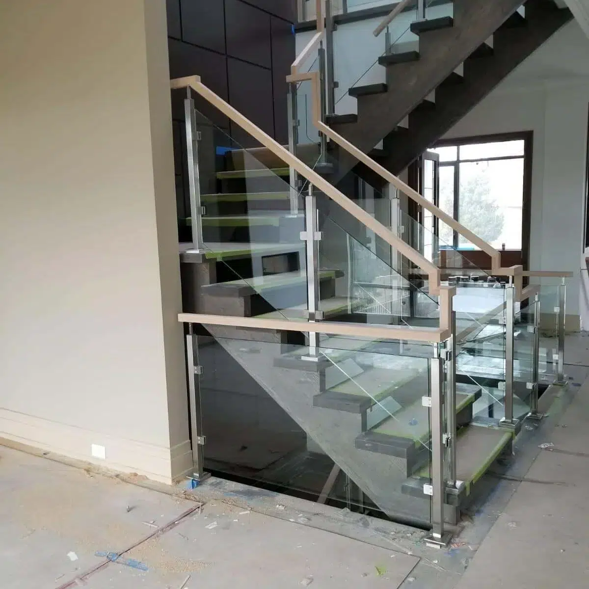 Framed Glass Railing with Stainless Posts Framed glass railing with stainless steel posts, glass clamps and a light wood handrail in a new build under construction