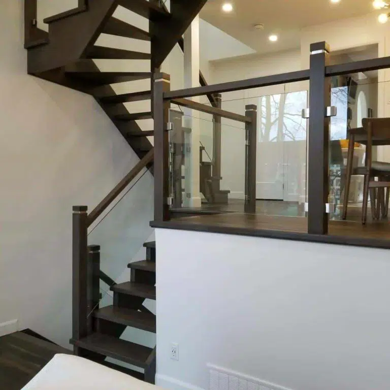 Framed Glass Railing with Wood Posts Framed glass railing with dark wood posts and stainless steel clamps around an open riser staircase and raised landing