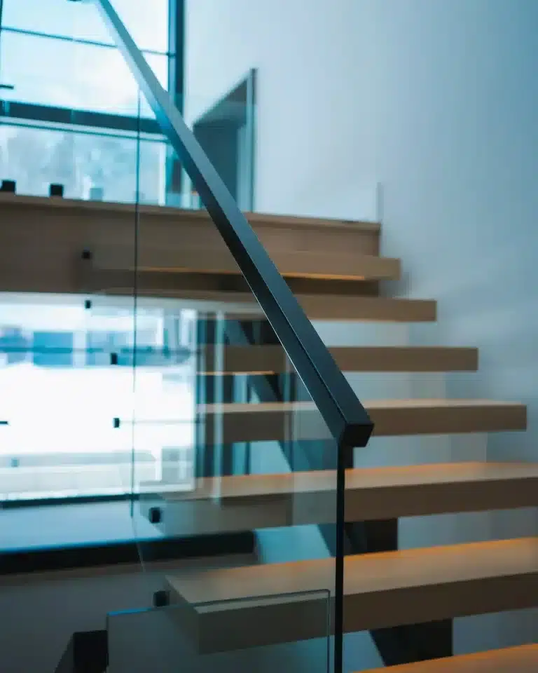 Frameless Glass Railing Close Up Close up of frameless glass railing with a black square handrail beside floating oak treads near a large window c