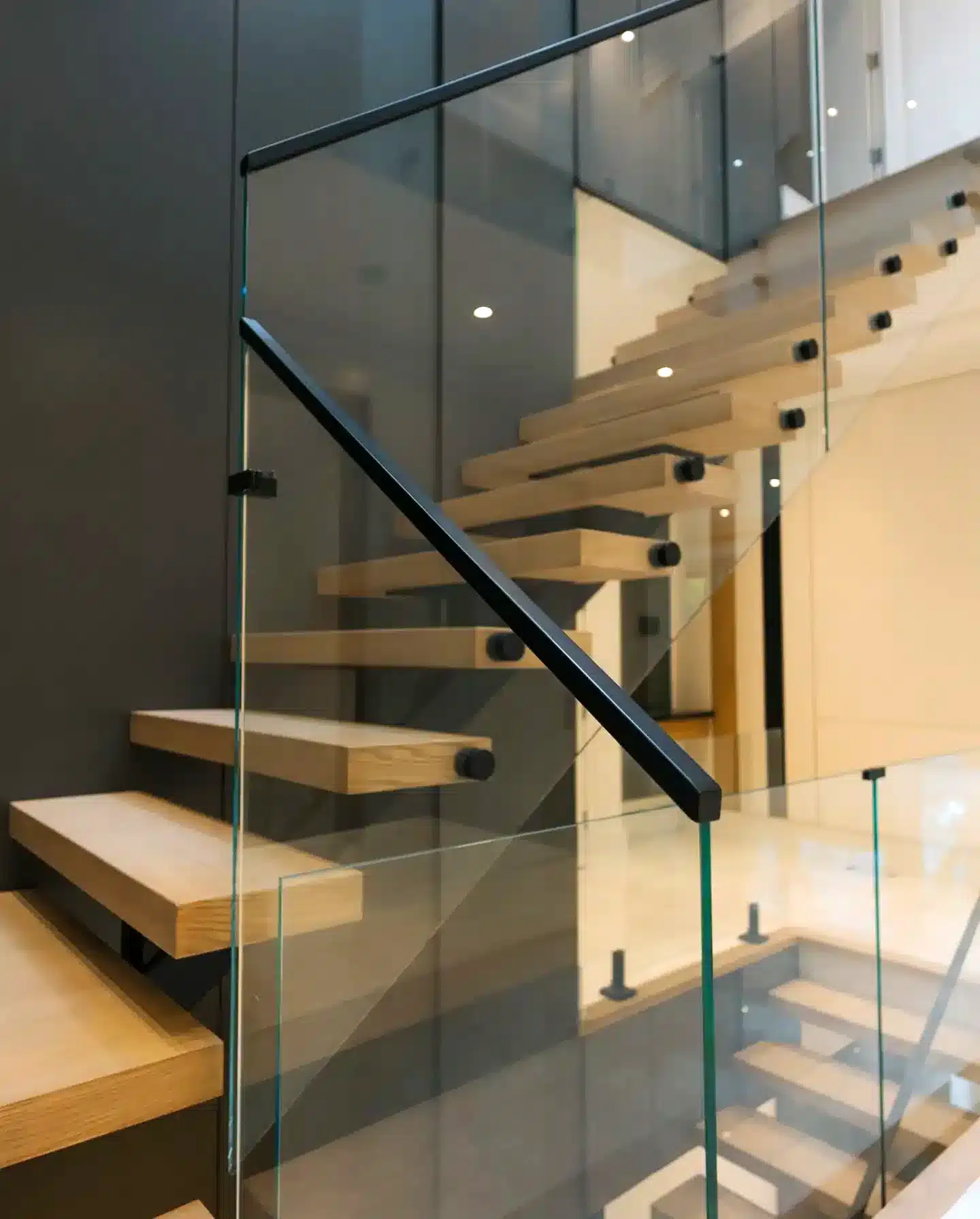 Frameless Glass Railing with Floating Treads Frameless glass railing with a slim black handrail beside floating oak treads anchored to a dark feature wall
