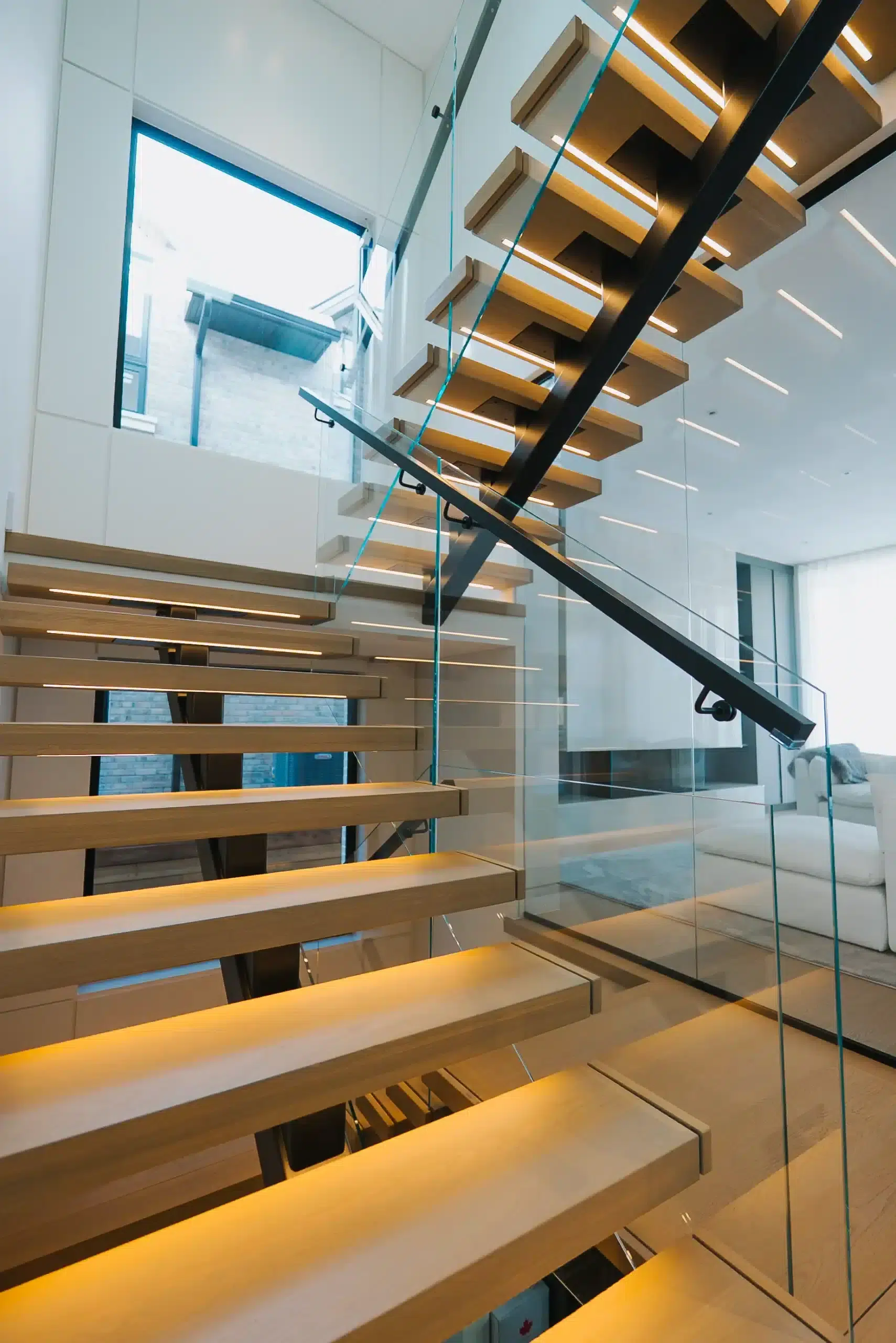 Frameless Glass Railing on Floating Stairs Frameless glass railing with a black handrail beside a floating oak staircase with LED lit treads