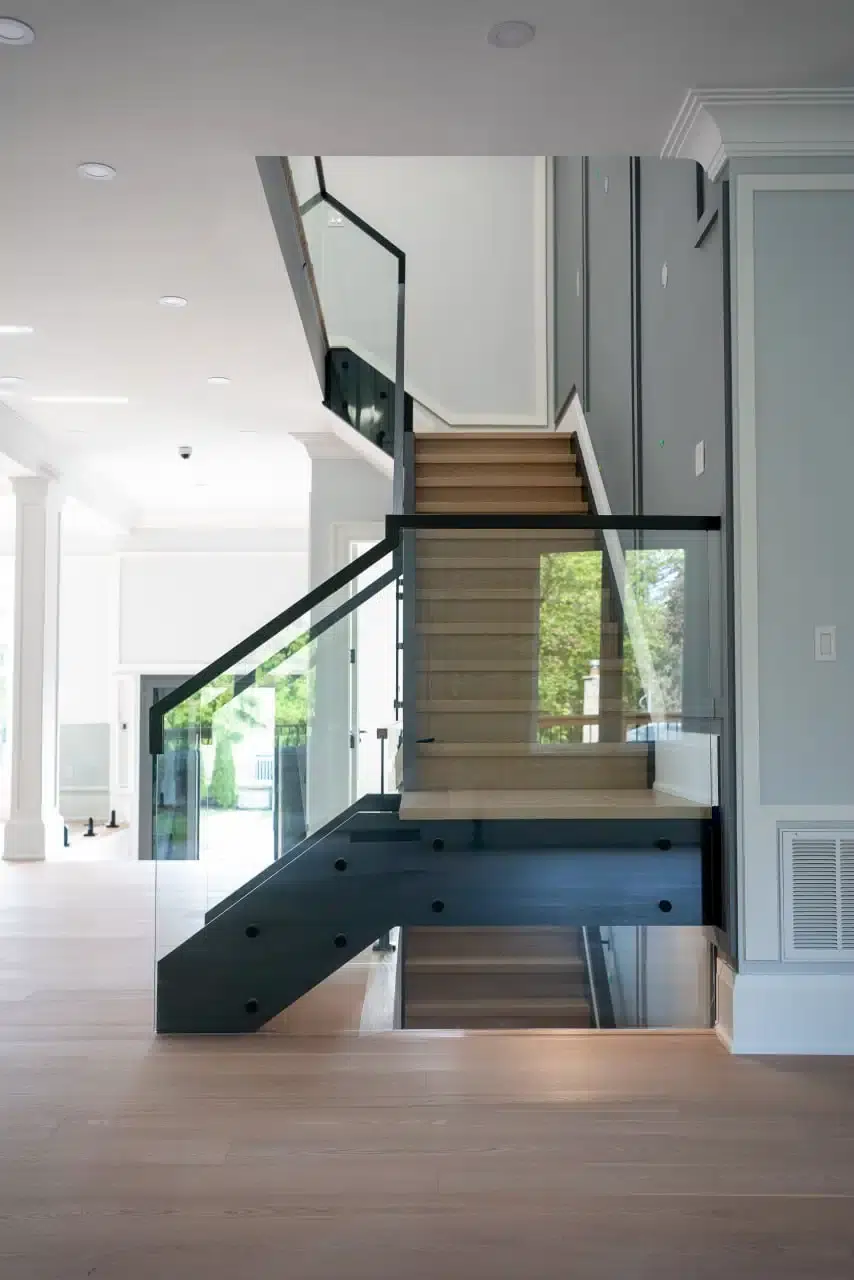 Glass Railing with Black Standoffs Glass railing with black standoffs and handrail on a U-shaped white oak staircase with garden views through the glass