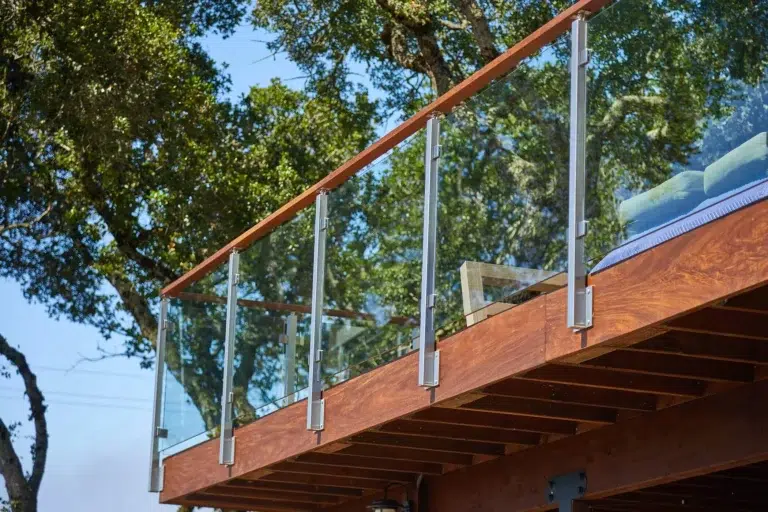 Glass railing with side-mounted stainless steel posts and a wood handrail on a raised outdoor wood deck