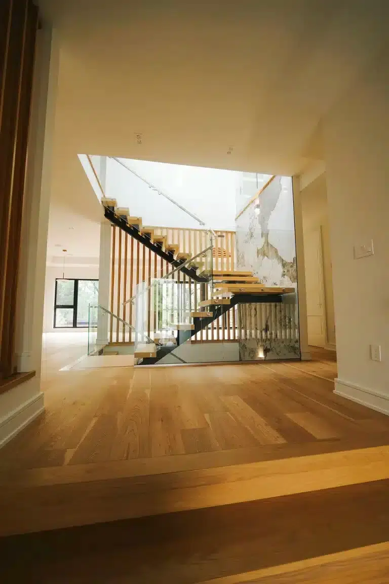 Glass Railing with Marble Feature Wall Floating oak staircase with glass railing and a stainless steel handrail beside a marble feature wall and wood slat screen