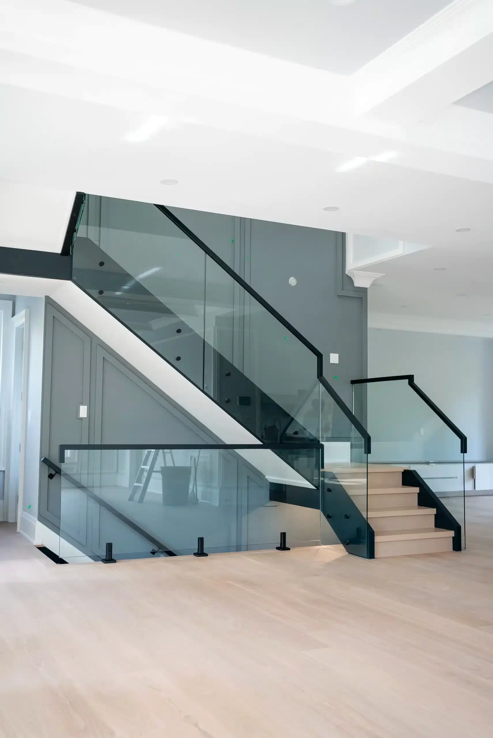 Glass Railing Systems for Open Stairwells Glass railing system with black handrails wrapping an open stairwell and white oak stairs in a new custom home