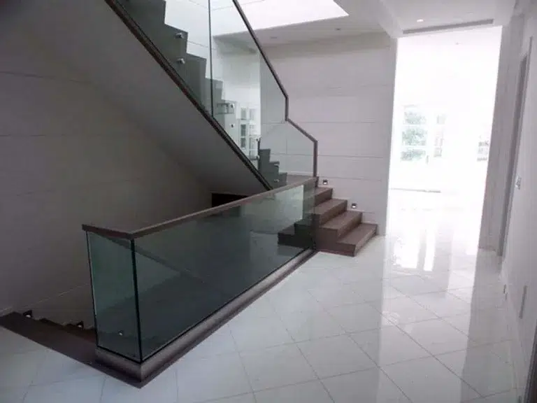 Glass railing with a wood top rail along a staircase and around the main floor stair opening in a bright hallway with white tile floors