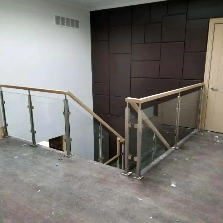 Hybrid glass railing with stainless steel posts, glass clamps and a light wood handrail around a stair opening during construction